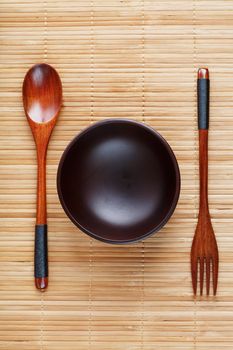 Natural wood plate, spoon and fork on a bamboo backing. Asian food handicraft concept. View from above