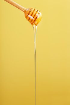 Honey drips in a thin stream from a honey dipper on a yellow background. Healthy food diet concept, ecologically pure product