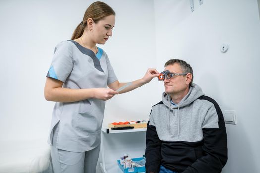 Vision correction. Selection of eyeglasses. Professional trial frames on male patient face while doctor checks eyesight in modern ophthalmologist office. Optometrist checking prescription for glasses.