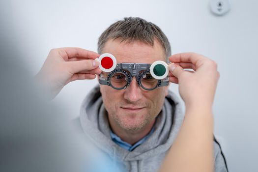 Male patient undergoes an eye test and prescription for eyeglasses in ophthalmology clinic. Optometrist checking patient eyesight and vision correction. Changing lenses on trial frame on patient nose.