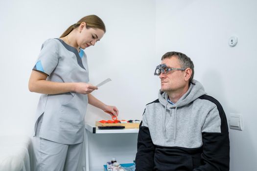 Vision correction. Selection of eyeglasses. Professional trial frames on male patient face while doctor checks eyesight in modern ophthalmologist office. Optometrist checking prescription for glasses.