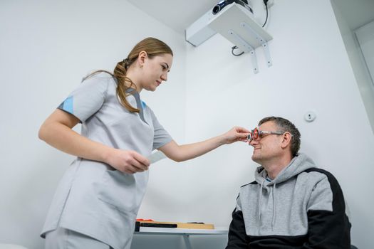 Male patient undergoes an eye test and prescription for eyeglasses in ophthalmology clinic. Optometrist checking patient eyesight and vision correction. Changing lenses on trial frame on patient nose.