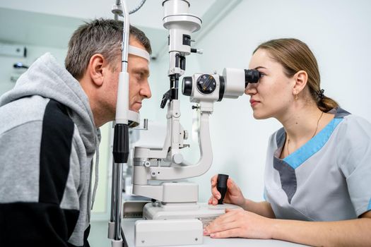 Ophthalmologist and patient testing eyesight. Man doing eye test with optometrist. Ophthalmologist using apparatus for eye examination in clinic. Doctor examining patient doing eyesight measurement.