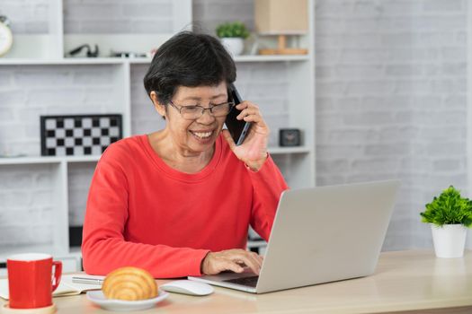 Smiling elderly woman on the phone, talking on business, in home office, retired woman working from home. Business concept.