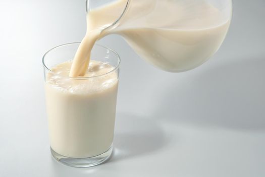 Almond milk is poured from a transparent jug into a glass. on gray background.