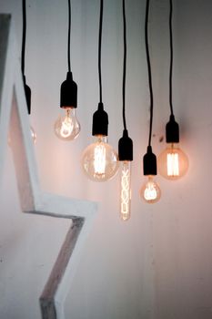 Hanging edison light bulbs on black strings on white wall background