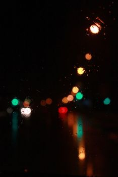 Car traffic lights bokeh through rainy window glass on black background. Defocused city night colorful round lights. 