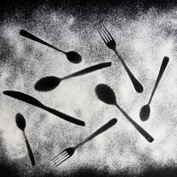 the imprint of some cutlery on a black surface sprinkled with flour