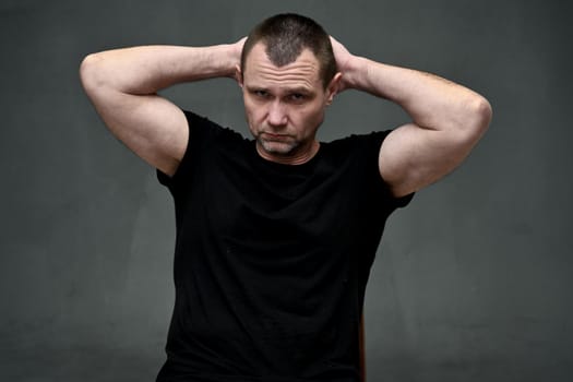 Portrait of an adult caucasian man holding his hands behind his head on a gray background looking at the camera