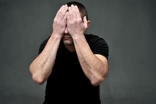 Adult caucasian man closed his eyes with his hands on a gray background