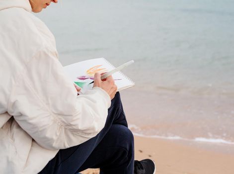 Hobbbies and leisure. young woman artist painting or doing travel sketches using watercolor sitting on the beach