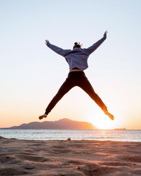 Health and wellness. Young woman in sport clothes enjoying sunrise standing at the beach, doing workout jumping high