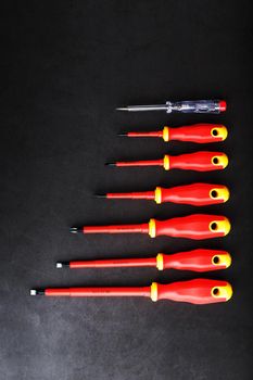 A set of red screwdrivers in a row on a black background. Top view, free space