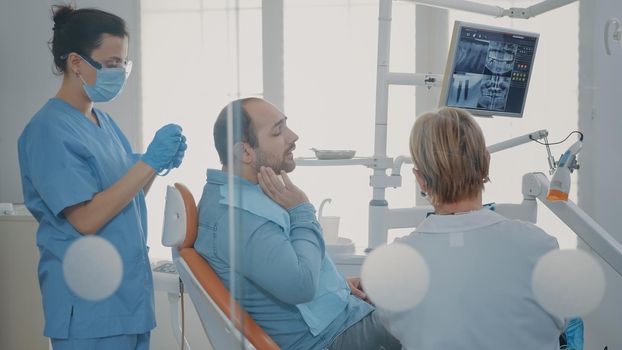 Dentist showing teeth radiography to patient on dental chair, preparing for stomatological procedure with drill tools. Stomatologist holding x ray scan results before denture inspection.