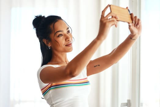 Cropped shot of an attractive young blogger standing in her home and using her cellphone to take a selfie