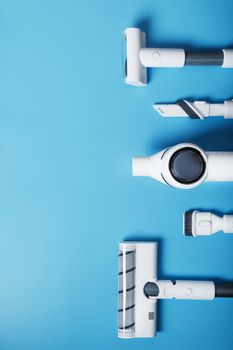 A set of nozzles and a white cordless vacuum cleaner in a row on a blue background. Top view