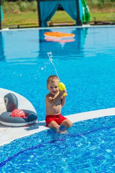 the child sits near the pool is played with a water pistol. selective focus