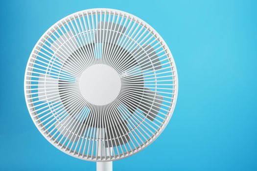 Electric fan in white with a modern design for cooling the room on a blue background. Free space, minimalistic style.