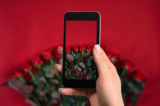 Closeup of woman is preparing to make a photo with a mobile phone. Bouquet of roses on a red background. Top view