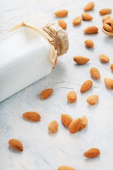 Almond milk in a glass bottle on a light background with a scattering of seed kernels and a wooden spoon. Top view