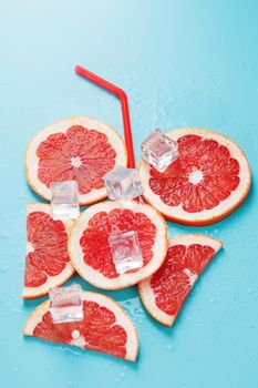 A composition of grapefruit slices and ice cubes with a blue background in the form of a refreshing drink. Top view, free space