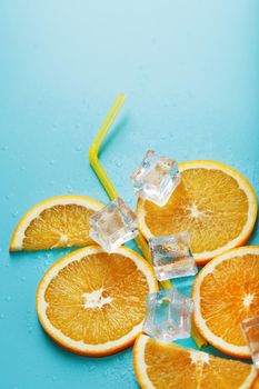 Orange slices and ice cubes with a straw on a blue background in the shape of a cocktail. The concept of the drink lemonade is a summer refreshing composition. Top view