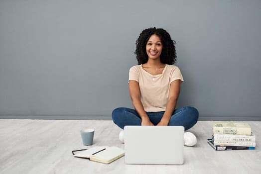 Studio shot of a young woman using a laptop while completing her studies against a gray background