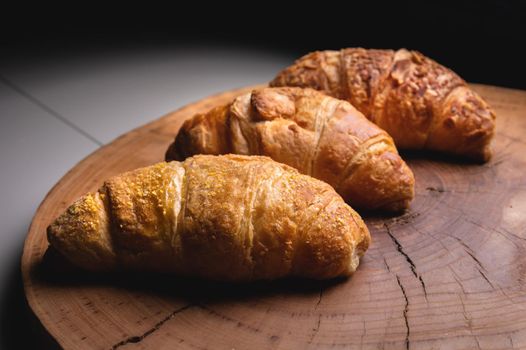 Several Croissants on a cutting board made of sawn wood on a dark background. Healthy and tasty breakfast.