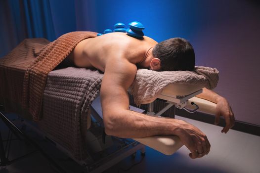 Man lying down recovering health with vacuum cups. Close-up of vacuum cups on the back of a man against a black-blue background. Traditional oriental medicine