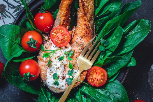 A plate with fresh green raw spinach and fried wild salmon, tomatoes and cream cheese sauce High quality photo