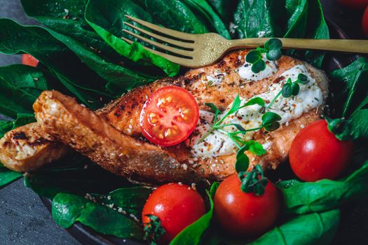 A plate with fresh green raw spinach and fried wild salmon, tomatoes and cream cheese sauce High quality photo