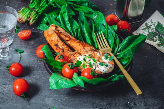 A plate with fresh green raw spinach and fried wild salmon, tomatoes and cream cheese sauce High quality photo