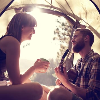 Shot of a young man playing guitar to his girlfriend in a tent