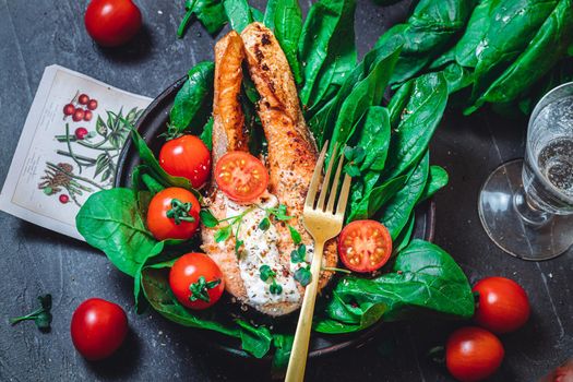 A plate with fresh green raw spinach and fried wild salmon, tomatoes and cream cheese sauce High quality photo