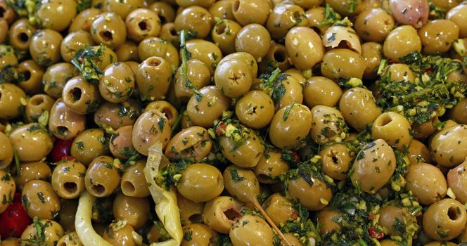 Close up background of traditional artisanal pickled green olives with spice herbs on retail display of open market, high angle view