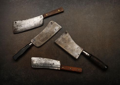 Close up vintage butcher meat cleavers on cutting board or grunge brown stone table surface with copy space, elevated top view, directly above