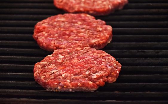 Close up raw beef or pork meat barbecue burgers for hamburger cooked on bbq grill, high angle view