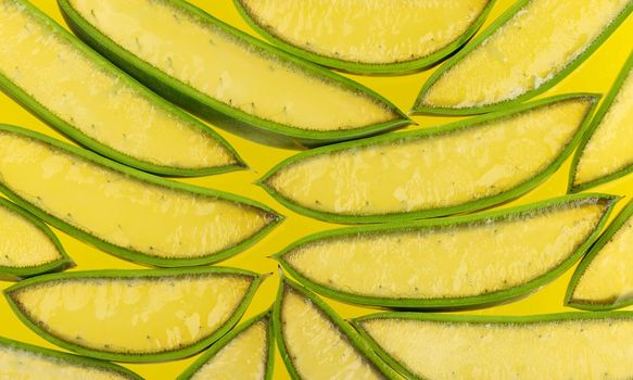 Close up background of fresh green Aloe Vera slices full of juicy gel on yellow, high angle view, directly above