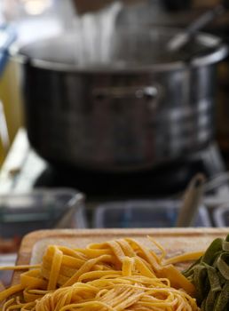 Close up cooking fresh handmade traditional Italian tagliatelle pasta, uncooked black, green and classical past on wooden table, high angle view