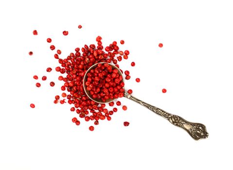 Close up one vintage metal spoon full of red pink pepper peppercorns spilled and spread around isolated on white background, elevated top view, directly above