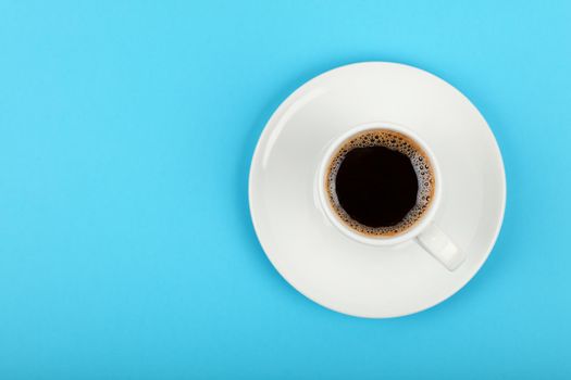Close up one white cup full of black coffee on saucer over blue background, elevated top view, directly above