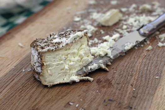 Close up one cut fresh French artisan gourmet goat cheese with herb spices and knife on wooden cutting board, high angle view