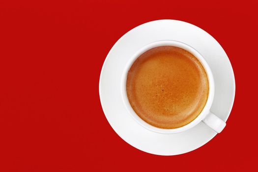 Close up one full cup of espresso coffee and white saucer over vivid red background, elevated top view, directly above