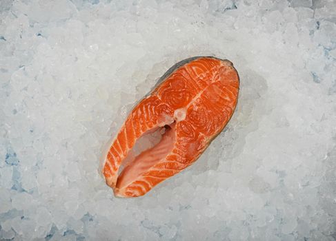 Close up one fresh raw salmon fish steak on background of crushed ice on retail display, elevated top view, directly above