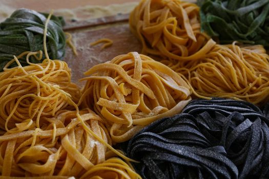 Close up cooking fresh handmade traditional Italian tagliatelle pasta, uncooked black, green and classical past on wooden table, high angle view