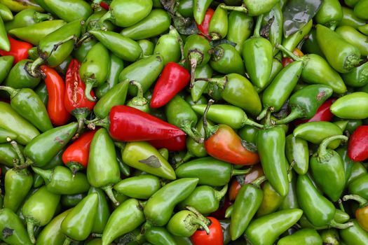 Close up heap of many fresh green and red hot jalapeno chili peppers on retail display at farmers market, elevated top view, directly above