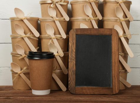 Close up brown paper coffee cup and empty blank black slate chalkboard sign over stack of desserts at coffee shop retail display