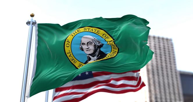 the flag of the US state of Washington waving in the wind with the American flag blurred in the background. Washington is a state in the Pacific Northwest region of the Western United States