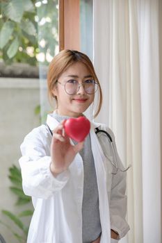 Portrait young asian beautiful doctor with stethoscope holding heart while standing at her office