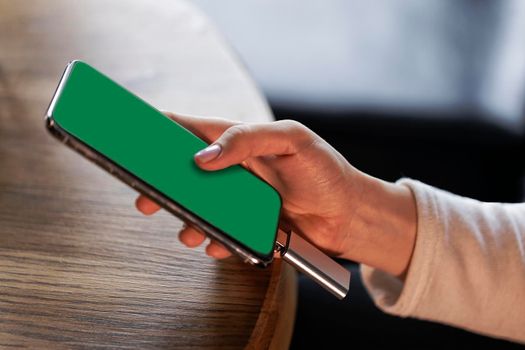 in a cafe at a table, a woman's hand holds a phone with a green screen in her hand close-up
